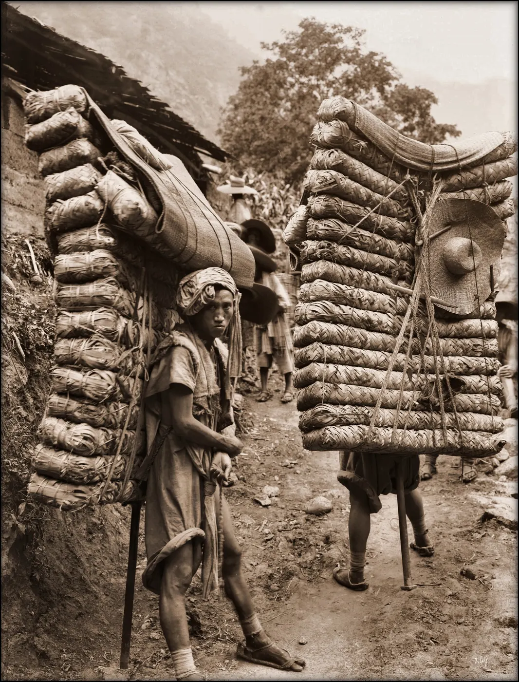 1908 photograph of two men carrying packaged brick tea in Sichuan, China