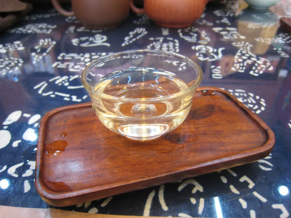 A glass cup of pale green tea on a wooden tray during tea tasting in Shanghai, China
