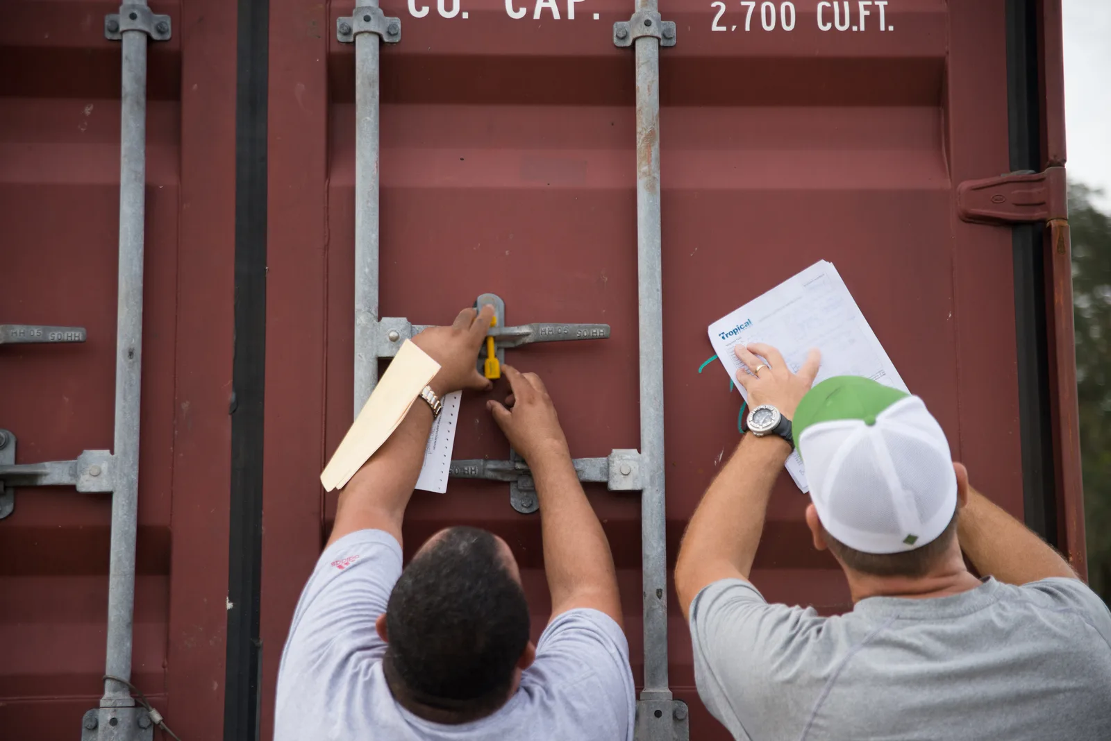 Two people applying and recording a security seal on a freight container